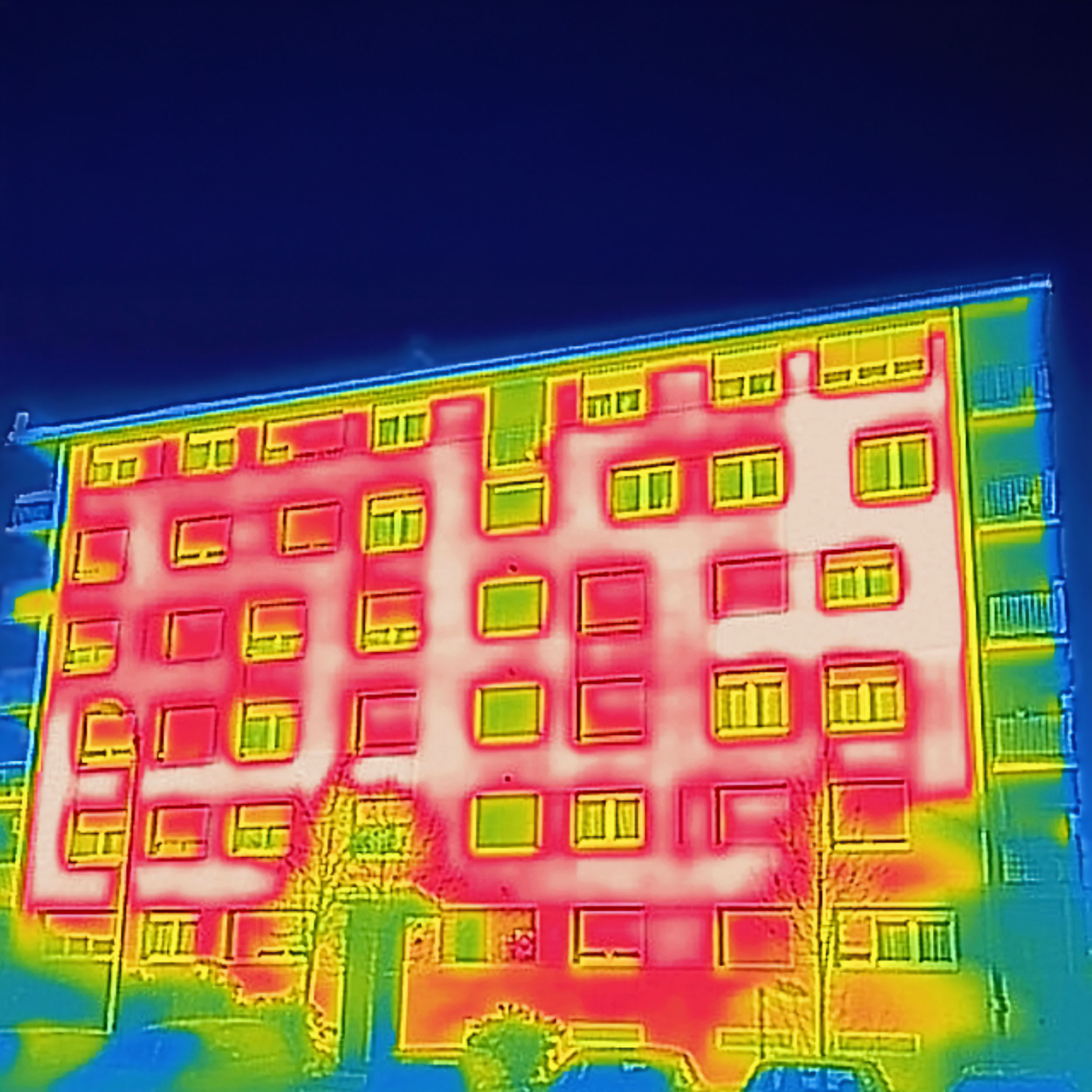 Thermografische Aufnahme eines Mehrfamilienhauses, die Wärmeverluste an der Fassade und den Fenstern visualisiert. Ein Symbol für den ersten Schritt zur energetischen Fassadensanierung.